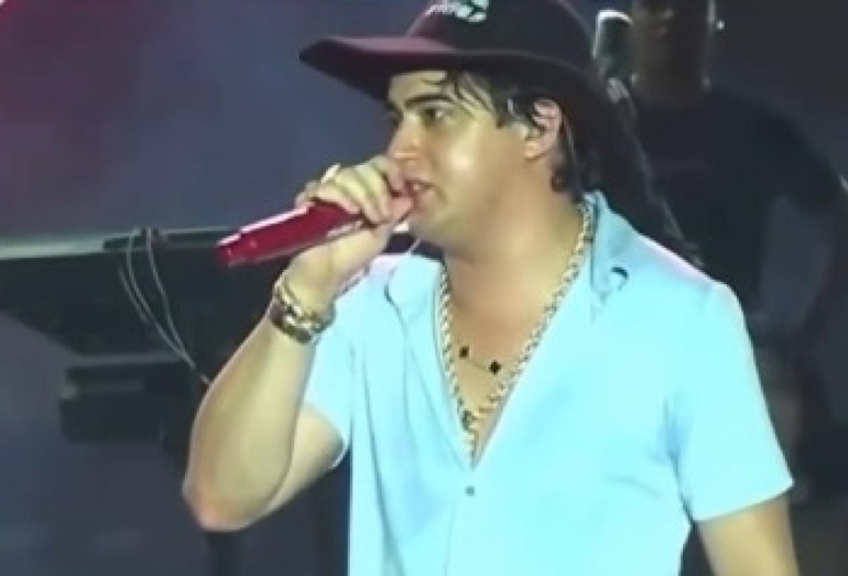 O cantor Natanzinho Lima segurando o microfone e falando com o público com expressão de choro e cansaço.