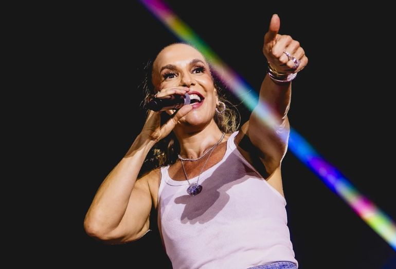 Ivete Sangalo cantando samba no palco, sorridente, cercada por músicos de apoio.