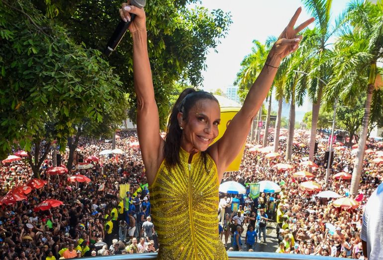 A cantora Ivete Sangalo em cima de um trio elétrico, com as mãos para o céu e expressão emocionada, cercada por uma multidão no Centro do Rio.